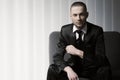 Elegant young fashion man in tuxedo on a sofa, blinds background Royalty Free Stock Photo