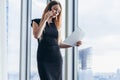 Elegant young female business owner holding documents talking on mobile phone discussing contract conditions standing in Royalty Free Stock Photo