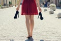 Elegant young girl in red dress with high-heels in hands, walking on the street barefoot. She is coming back home after party in Royalty Free Stock Photo