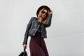 Elegant young hipster woman in a luxury hat in sunglasses in a leather jacket in pants with a backpack with a cape traveling Royalty Free Stock Photo