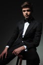 Elegant young man in tuxedo sits on wooden chair Royalty Free Stock Photo