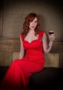 Elegant young redhead woman in a red dress, having a glass of red wine Royalty Free Stock Photo