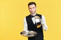 Elegant young waiter holding cloche over empty tray ready to serve on yellow background