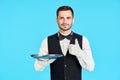 Elegant young waiter holding empty silver tray and showing thumbs up sign over blue background Royalty Free Stock Photo