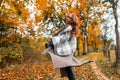 Elegant young woman in autumn stylish clothes is spinning in the park. Joyful girl model in a knitted scarf in a fashionable long