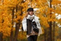 Elegant young woman in a chic hat in a stylish brown jacket with a leather bag with a scarf posing on the background of trees with Royalty Free Stock Photo