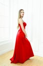 Elegant young woman in evening red dress posing on white wall background. Royalty Free Stock Photo