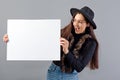 Elegant young woman in glasses and hat showing empty board banner, isolated on gray, copy space Royalty Free Stock Photo