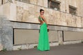 Elegant woman in green dress posing against a concrete wall