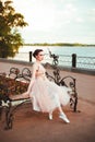 an elegant young woman in a princess dress is sitting in a pink dress on a bench on the river bank, a romantic wedding