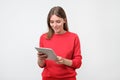 Elegant young woman in red sweater using tablet, looking at screen