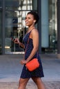 Elegant young woman walking outside with mobile phone and earphones