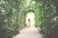 elegant young woman walks happily towards the exit of a tunnel formed by lush plants Royalty Free Stock Photo