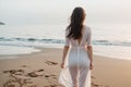 Elegant young woman with white dress walking by the beach in a warm sunset Royalty Free Stock Photo