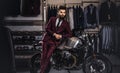 Handsome man with a stylish beard and hair dressed in vintage red suit posing near retro sports motorbike at men`s Royalty Free Stock Photo