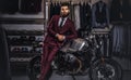 Handsome man with a stylish beard and hair dressed in vintage red suit posing near retro sports motorbike at men`s Royalty Free Stock Photo