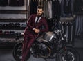 Handsome man with a stylish beard and hair dressed in vintage red suit posing near retro sports motorbike at men`s Royalty Free Stock Photo