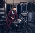 Handsome man with a stylish beard and hair dressed in vintage red suit posing near retro sports motorbike at men`s Royalty Free Stock Photo