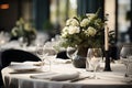 Elegantly set laid dining table with white roses in a dark vase, flanked by lit candles, creating an intimate and