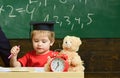 Elementary education concept. First former with toy on desk. Pupil in mortarboard, chalkboard on background. Boy on busy