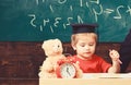 Elementary education concept. First former with toy on desk. Pupil in mortarboard, chalkboard on background. Boy on busy