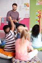 Elementary Pupils Raising Hands To Answer Question As Male Teacher Reads Story In Classroom Royalty Free Stock Photo