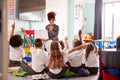 Elementary Pupils Wearing Uniform Raise Hands To Answer Question As Female Teacher Reads Book