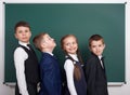 Elementary school boy near blank chalkboard background, dressed in classic black suit, group pupil, education concept