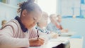 In Elementary School Classroom Black Girl Writes in Exercise Notebook, Taking Test. Junior Classro