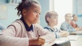 In Elementary School Classroom Black Girl Writes in Exercise Notebook, Taking Test. Junior Classro Royalty Free Stock Photo