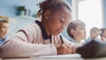 In Elementary School Classroom Black Girl Writes in Exercise Notebook, Taking Test. Junior Classro Royalty Free Stock Photo