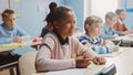 In Elementary School Classroom Brilliant Black Girl Writes in Exercise Notebook, Taking Test and W Royalty Free Stock Photo