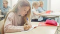 In Elementary School Classroom Caucasian Girl Writes in Exercise Notebook, Taking Test and Writing Royalty Free Stock Photo