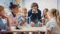 Elementary School Classroom: Enthusiastic Teacher Holding Tablet Computer Explains Lesson to Brill Royalty Free Stock Photo