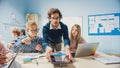 Elementary School Classroom: Enthusiastic Teacher Holding Tablet Computer Explains Lesson to Brill Royalty Free Stock Photo