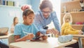 Elementary School Computer Science Class: Cute Girl Uses Digital Tablet Computer, Friendly Teacher Royalty Free Stock Photo