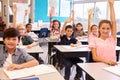 Elementary school kids in a classroom raising their hands Royalty Free Stock Photo