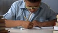 Elementary school pupil diligently writing letters in his notebook, calligraphy