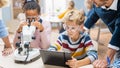 Elementary School Science Classroom: Cute Little Girl Looks Under Microscope, Boy Uses Digital Royalty Free Stock Photo