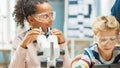 Elementary School Science Classroom: Cute Little Girl Looks Under Microscope, Boy Uses Digital Royalty Free Stock Photo