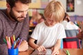 Elementary School Teacher And Male Pupil Drawing Using Digital Tablet In Classroom