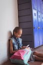 Elementary schoolgirl using mobile phone while sitting by lockers