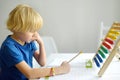 Elementary student boy doing homework at home. Child learning to count, solves arithmetic examples, doing exercises in workbook. Royalty Free Stock Photo