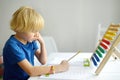 Elementary student boy doing homework at home. Child learning to count, solves arithmetic examples, doing exercises in workbook. Royalty Free Stock Photo