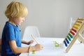 Elementary student boy doing homework at home. Child learning to count, solves arithmetic examples, doing exercises in workbook. Royalty Free Stock Photo