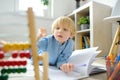 Elementary student boy doing homework at home. Child learning to count, solves arithmetic examples, using abacus. Math tutorial.