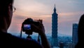 A man taking a picture of Taipei 101 during golden hour.