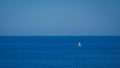 Solitude takes center stage as a lone sailing boat charts its course through the calm embrace of clear, azure waters.