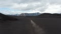 Elevated footage of fast moving and dusting car passing barren plains and riving volcanic ash. Mountain ridges in