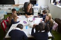 Elevated view of female primary school teacher sitting at table in a classroom with schoolchildren during a lesson Royalty Free Stock Photo